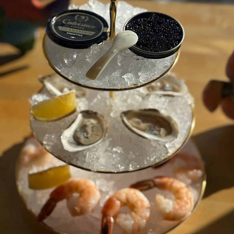 Three-tiered seafood tower with caviar, oysters, shrimp, and lemon wedges on ice.