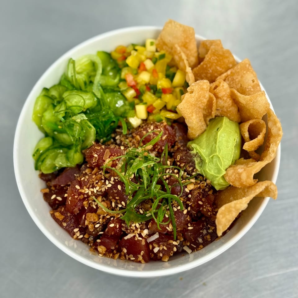 A vibrant poke bowl with tuna, mango salsa, seaweed salad, avocado, and crispy wonton chips.