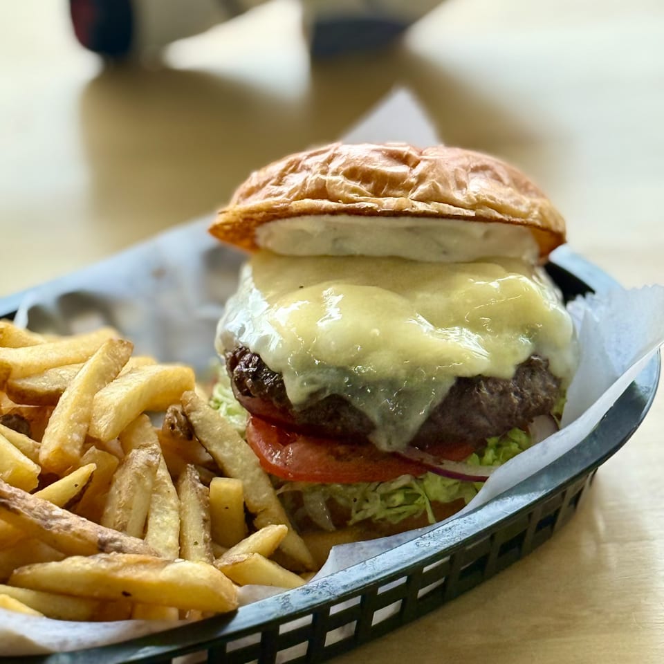 A cheeseburger with melted cheese, lettuce, tomato, and onion, served with fries in a black basket.