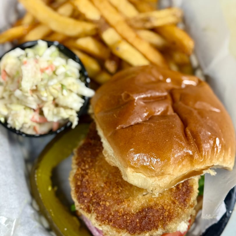 A fried chicken sandwich with coleslaw, french fries, and a pickle spear in a basket.