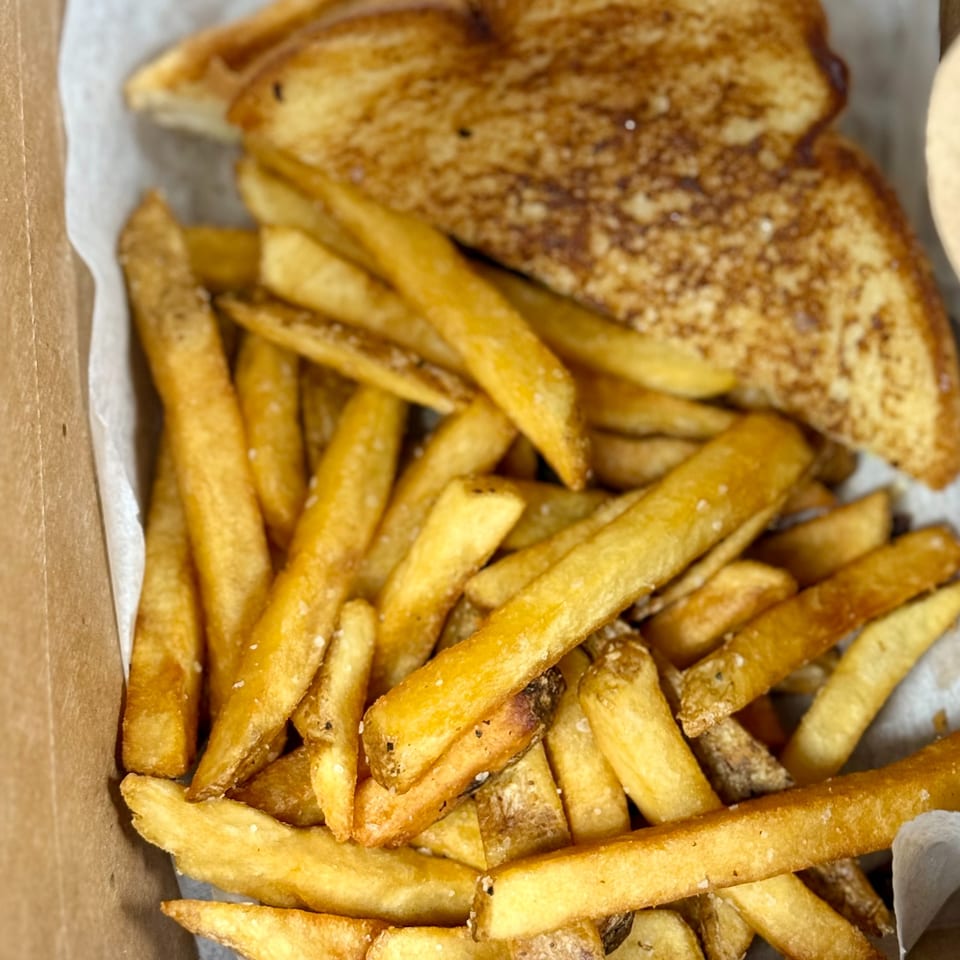 Golden french fries with salt and pepper, and a piece of toasted bread in a takeout box.