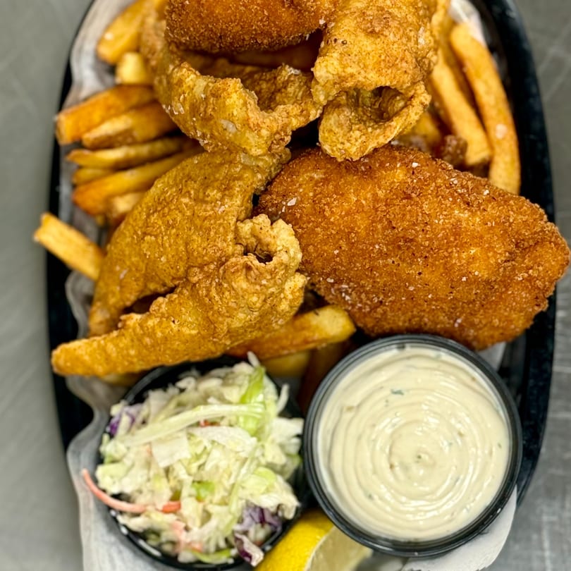 Crispy fried fish and french fries with coleslaw, tartar sauce, and a lemon wedge.