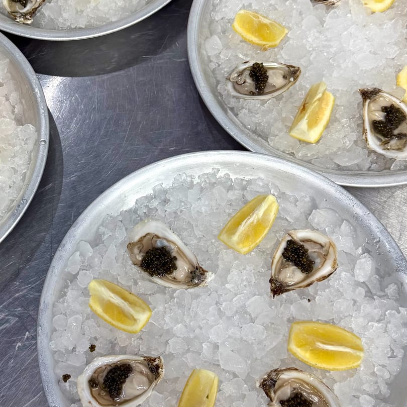 Plates of fresh oysters topped with caviar and lemon wedges, served on crushed ice.