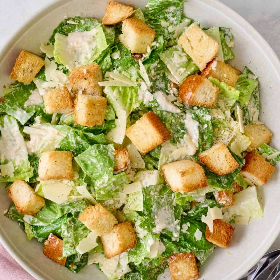 Close-up overhead view of a Caesar salad with romaine lettuce, croutons, and Parmesan cheese.