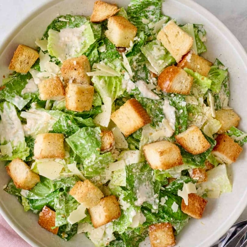 Close-up overhead view of a Caesar salad with romaine lettuce, croutons, and Parmesan cheese.